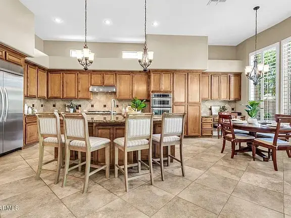 Spacious kitchen with wooden cabinets, island with bar stools, dining table, and stainless steel appliances.