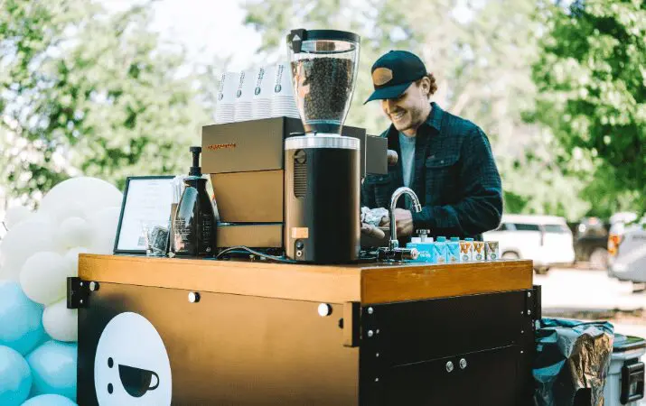 Barista preparing coffee at an outdoor mobile coffee cart surrounded by balloons.