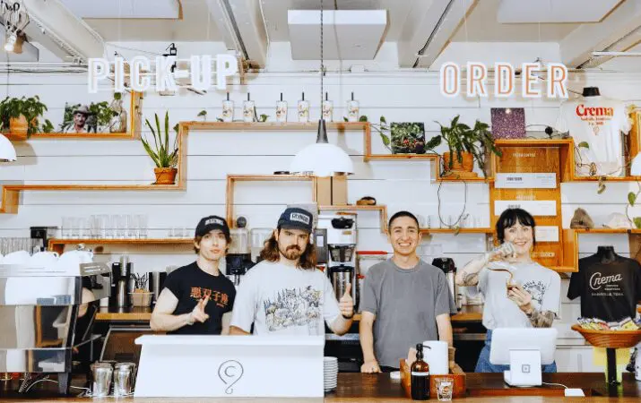 Four baristas behind a counter, with 'Pick Up' and 'Order' signs above them.