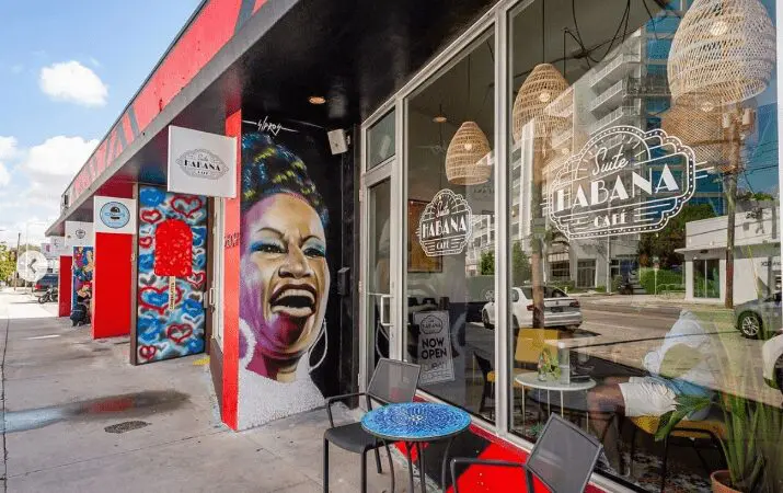Storefront of Suite Habana Cafe with a colorful mural of a smiling person on the wall.