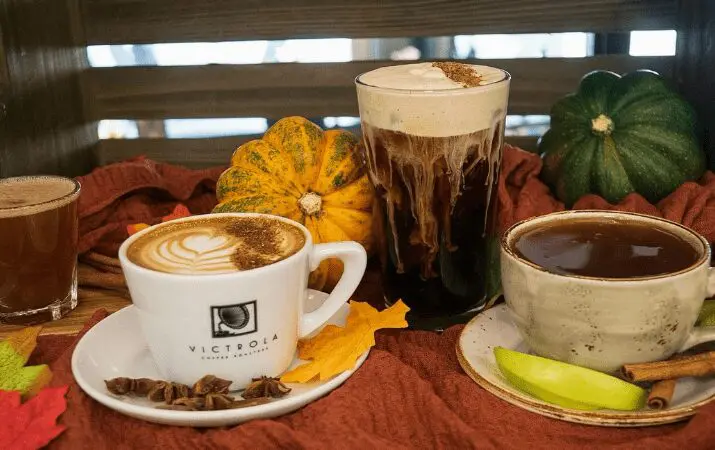 Coffee and tea drinks on a table with pumpkins and autumn leaves in the background.