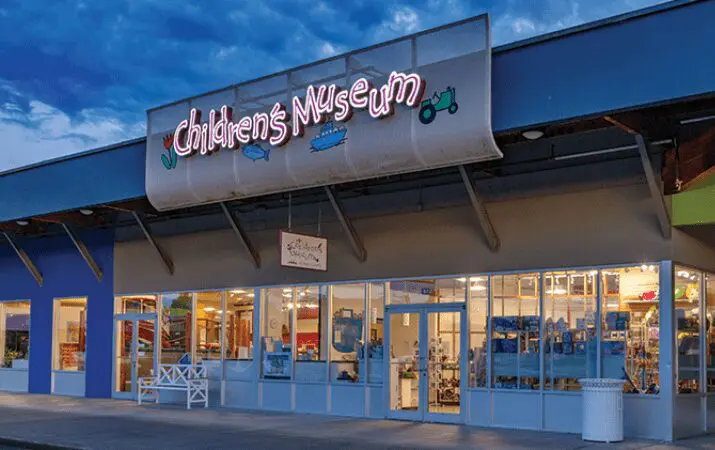 Exterior of a building with a neon sign reading 'Children's Museum' at dusk.