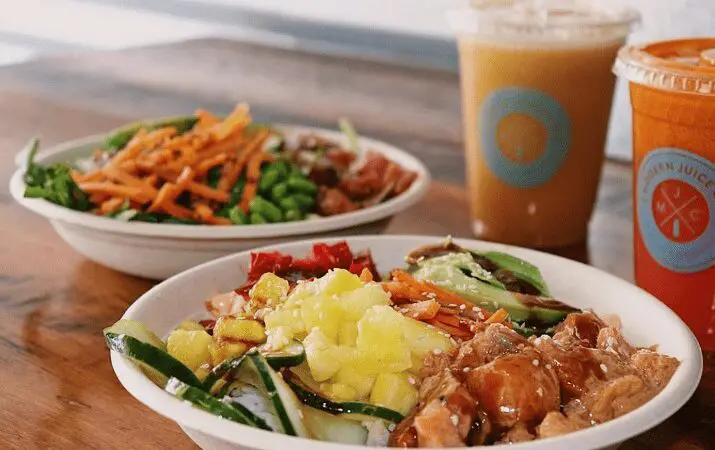 Bowls of salad with vegetables and chicken, accompanied by two iced drinks on a wooden table.