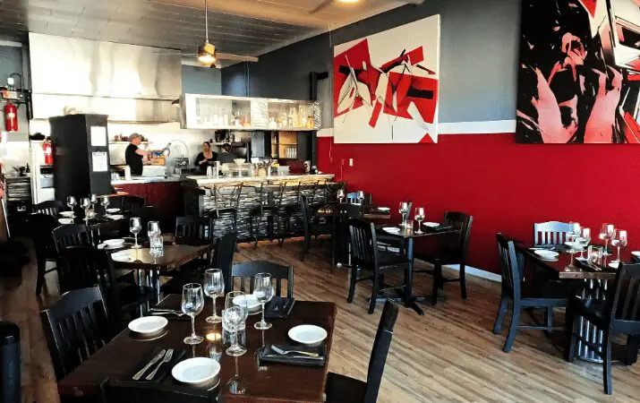 Casual restaurant interior with modern art, set tables, and an open kitchen in the background.