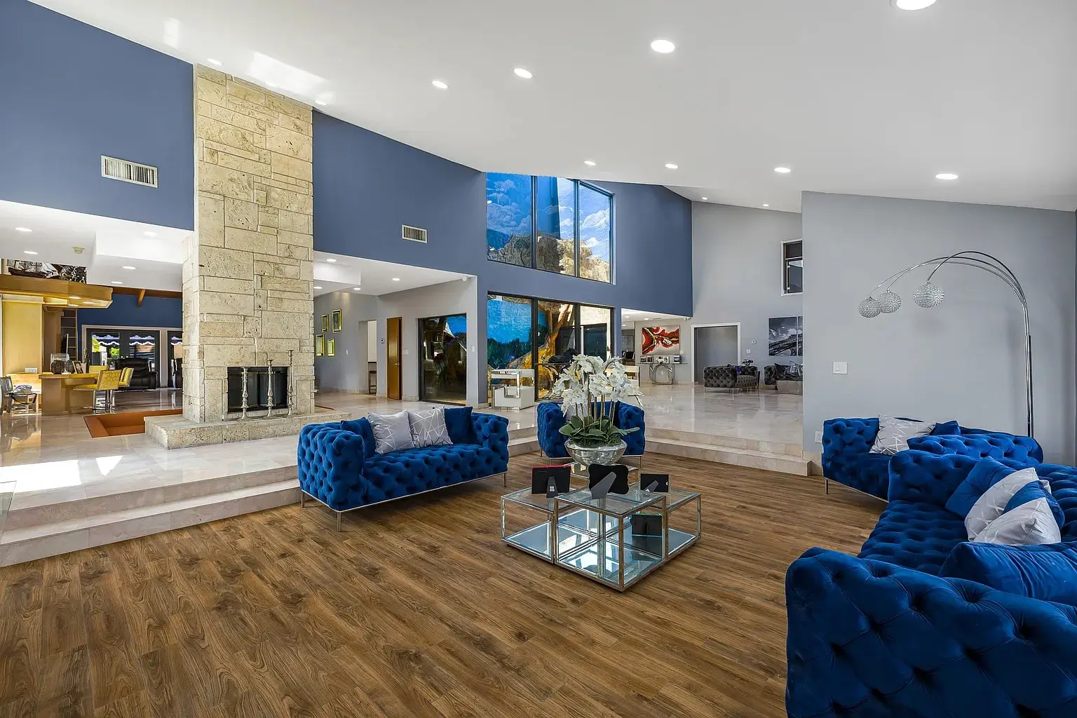Spacious modern living room with blue sofas, wooden floor, and large windows.