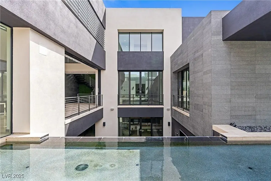 Modern building courtyard with large windows, gray walls, and a reflective water feature.