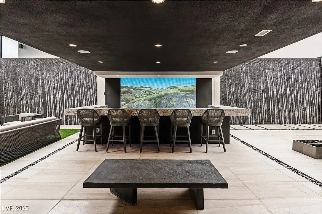 Modern outdoor bar area with high chairs, large TV, and sleek stone table.