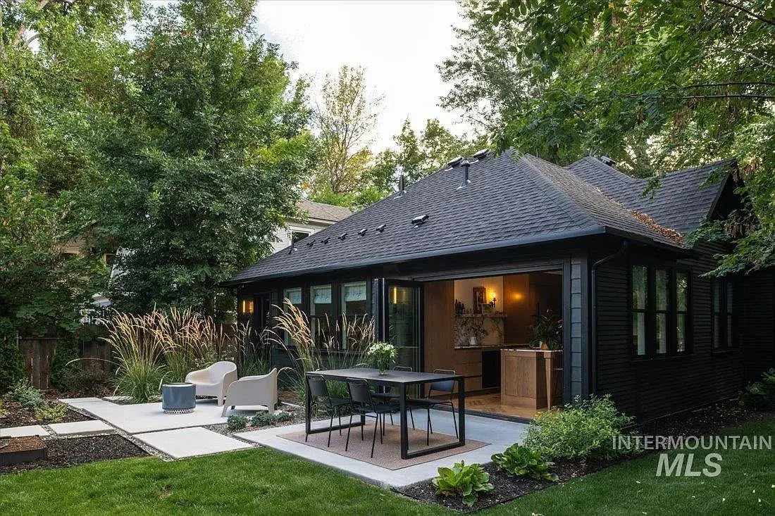 Modern backyard with a dark-colored house, open patio doors, outdoor seating, and lush greenery.
