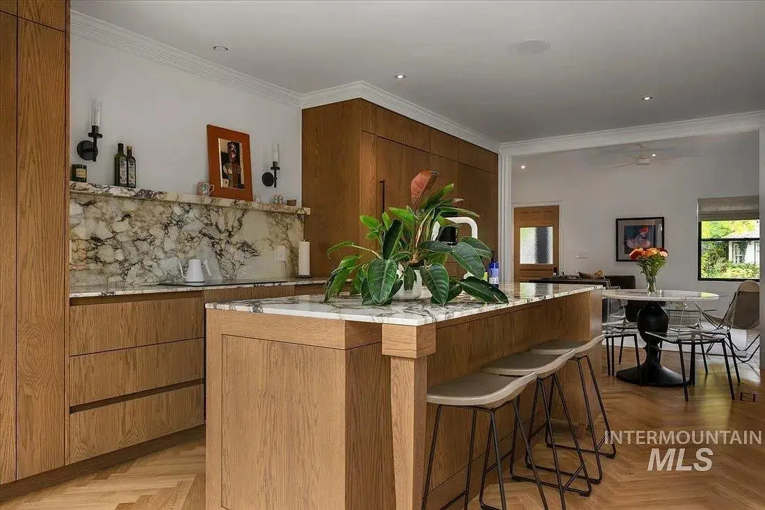 Modern kitchen with wooden cabinets, marble countertops, bar stools, and a large plant on the island.