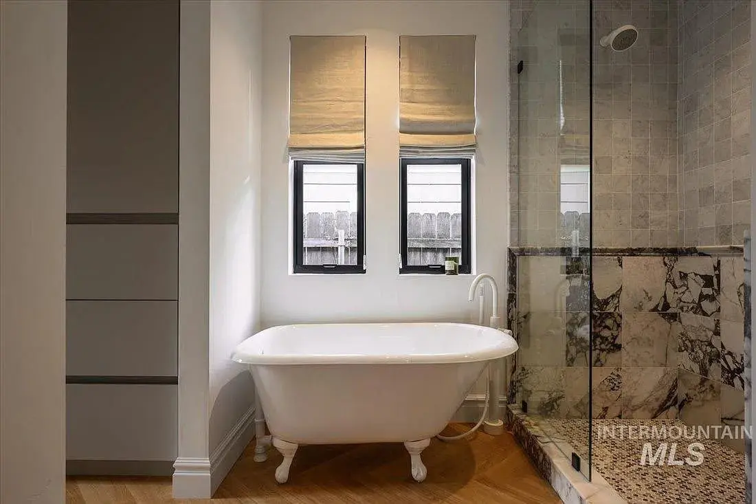 Clawfoot bathtub beside a glass-enclosed shower in a modern bathroom with natural light.