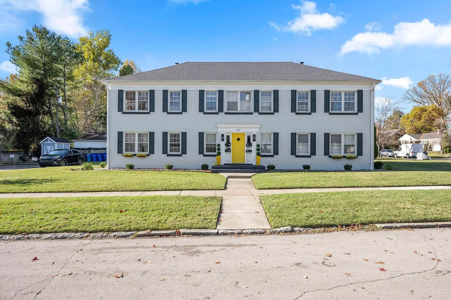 Two-story white house with yellow door, black shutters, and manicured lawn under a blue sky.