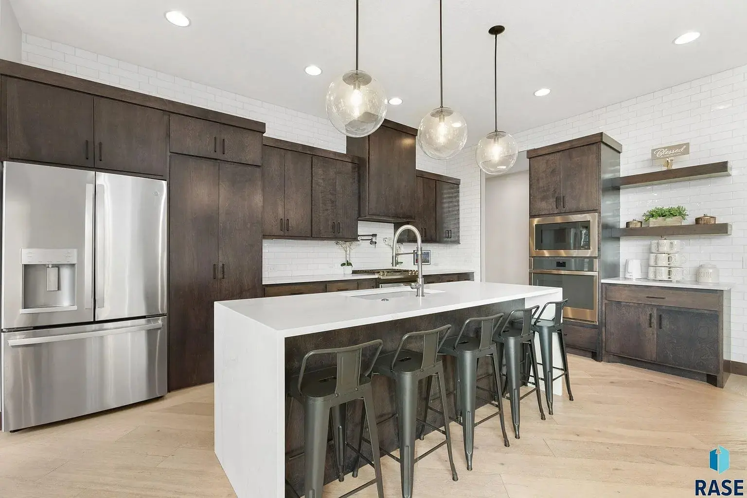 Modern kitchen with dark wood cabinets, white island, stainless steel appliances, and pendant lights.