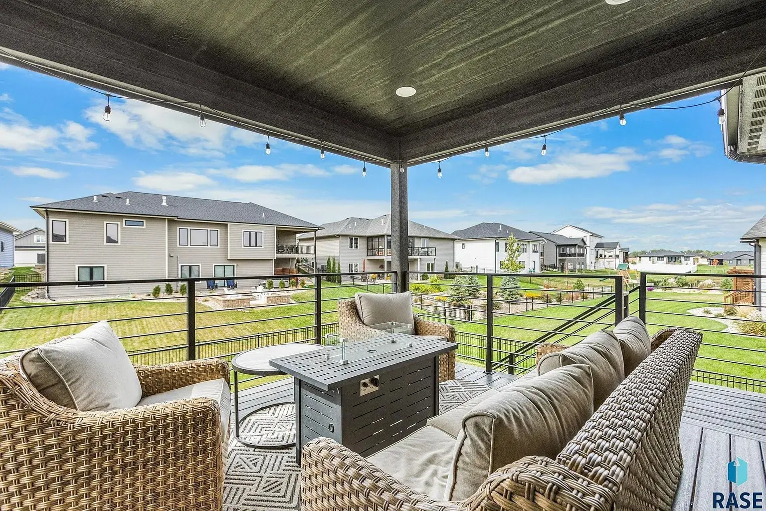 Covered patio with wicker furniture, fire pit table, and view of suburban neighborhood houses and lawns.
