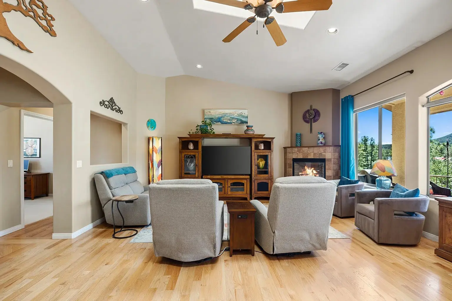Spacious living room with armchairs, TV, fireplace, and large windows overlooking greenery.