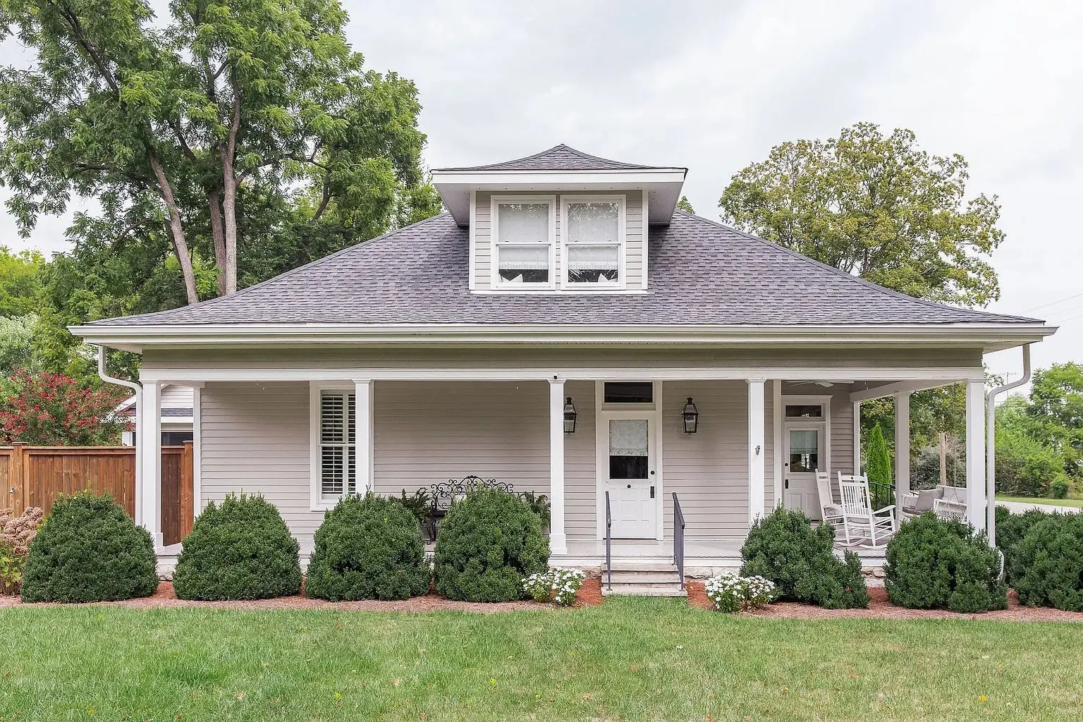 A charming single-story house with a covered porch, surrounded by bushes and trees.