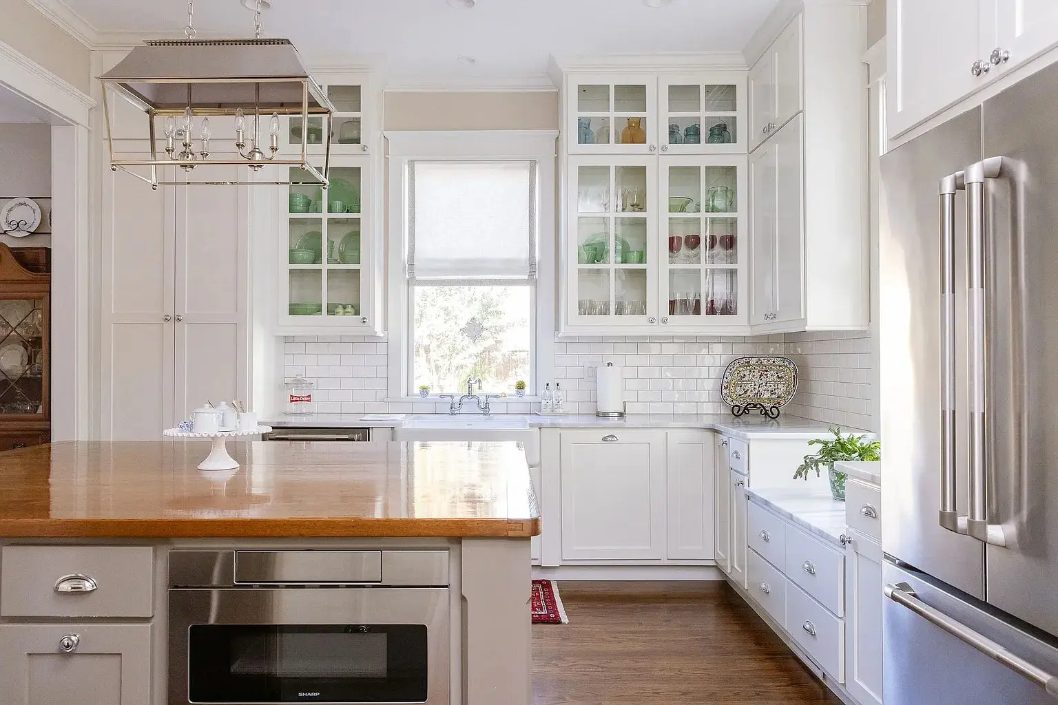 Modern kitchen with white cabinets, wooden island, stainless steel appliances, and glass-fronted upper cabinets.