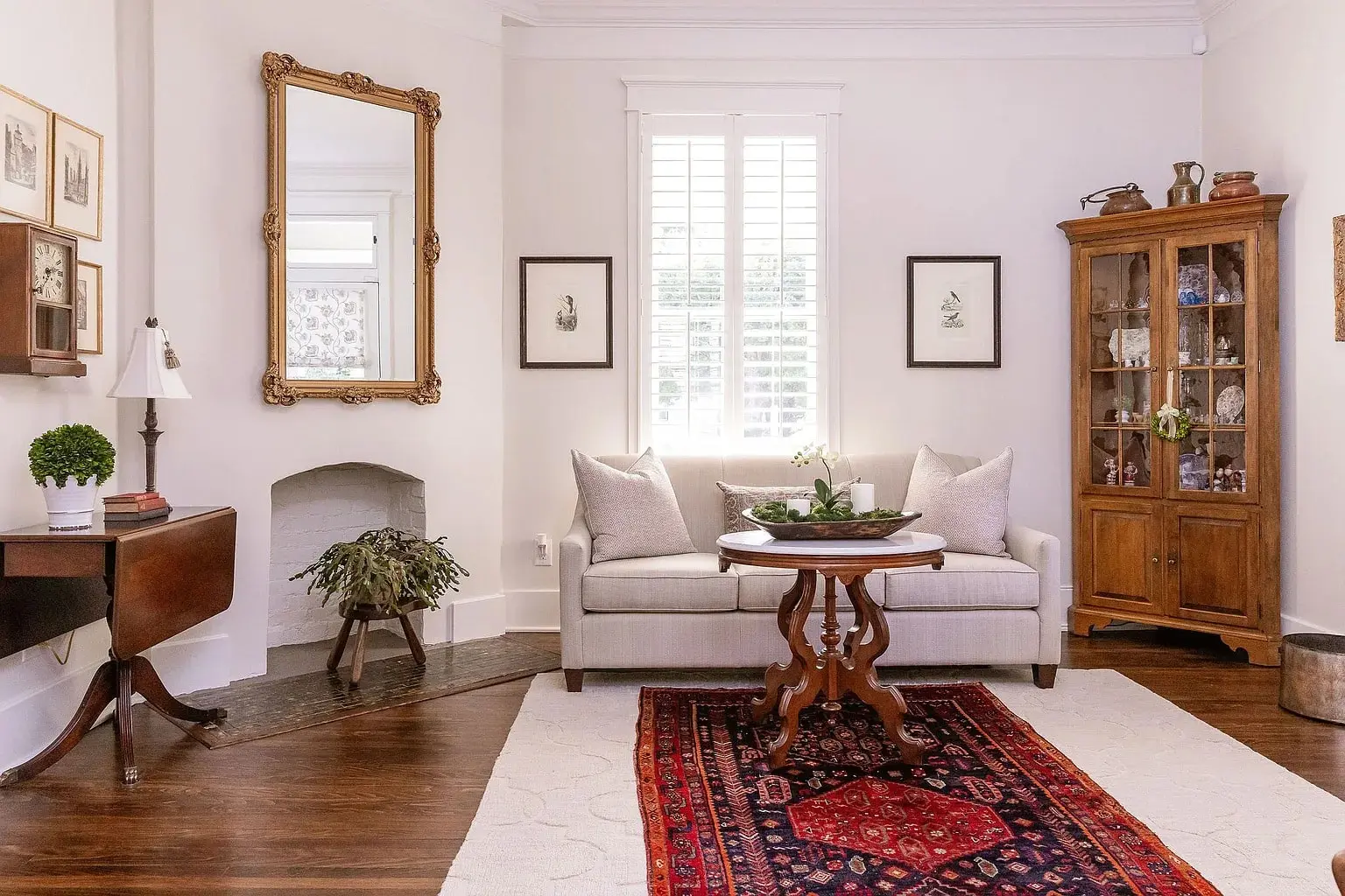 Elegant living room with a white sofa, wooden furniture, large mirror, and decorative rug.