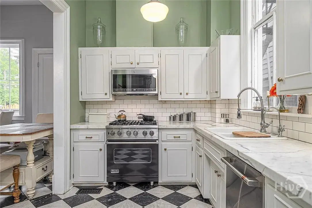 Modern kitchen with white cabinets, marble countertops, stainless steel appliances, and black-and-white checkered floor.