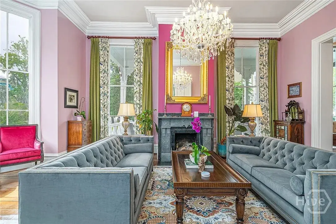 Elegant living room with pink walls, chandeliers, gray sofas, and a wooden coffee table.