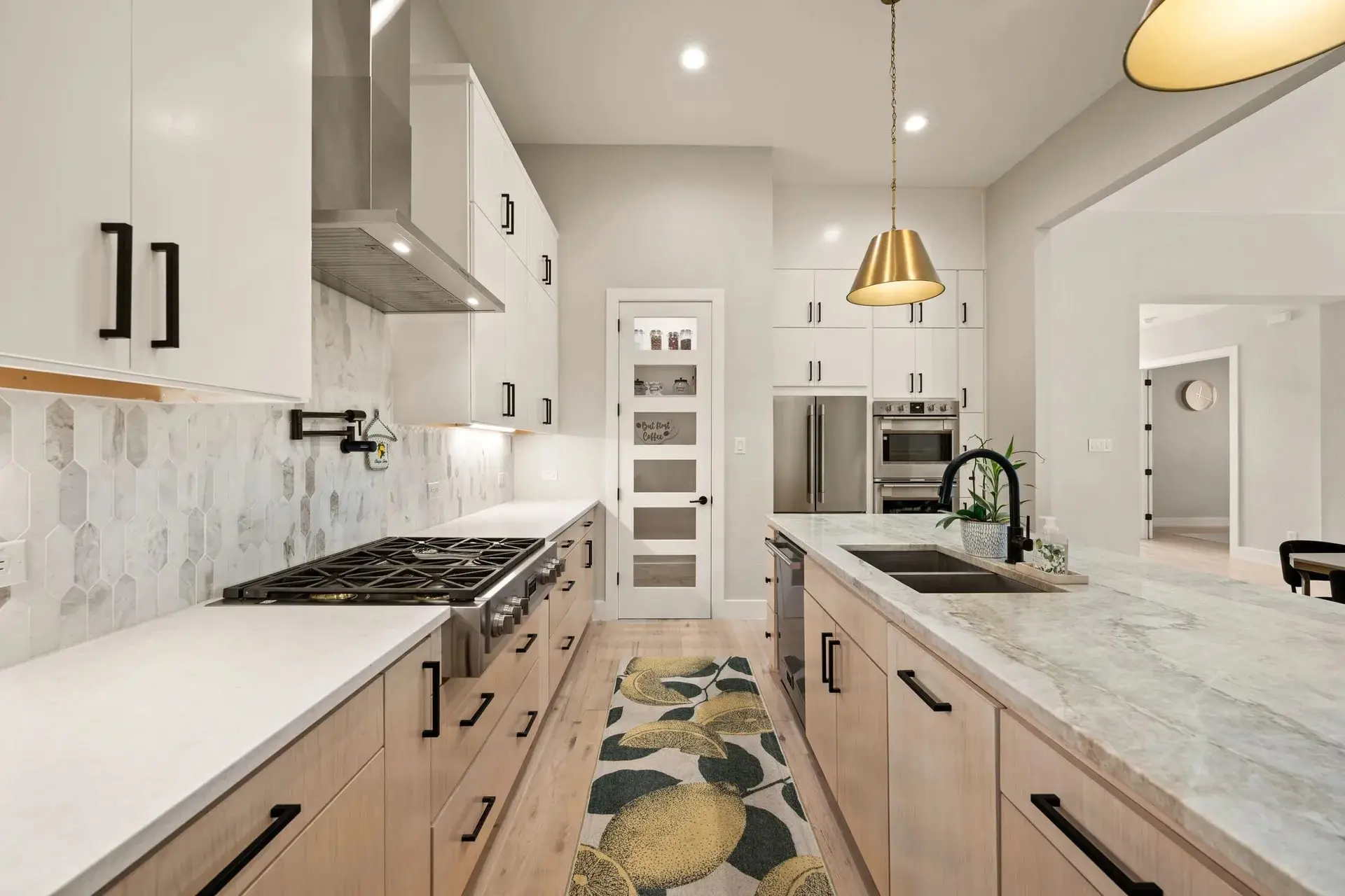 Modern kitchen with light wood cabinets, marble countertops, and stainless steel appliances.