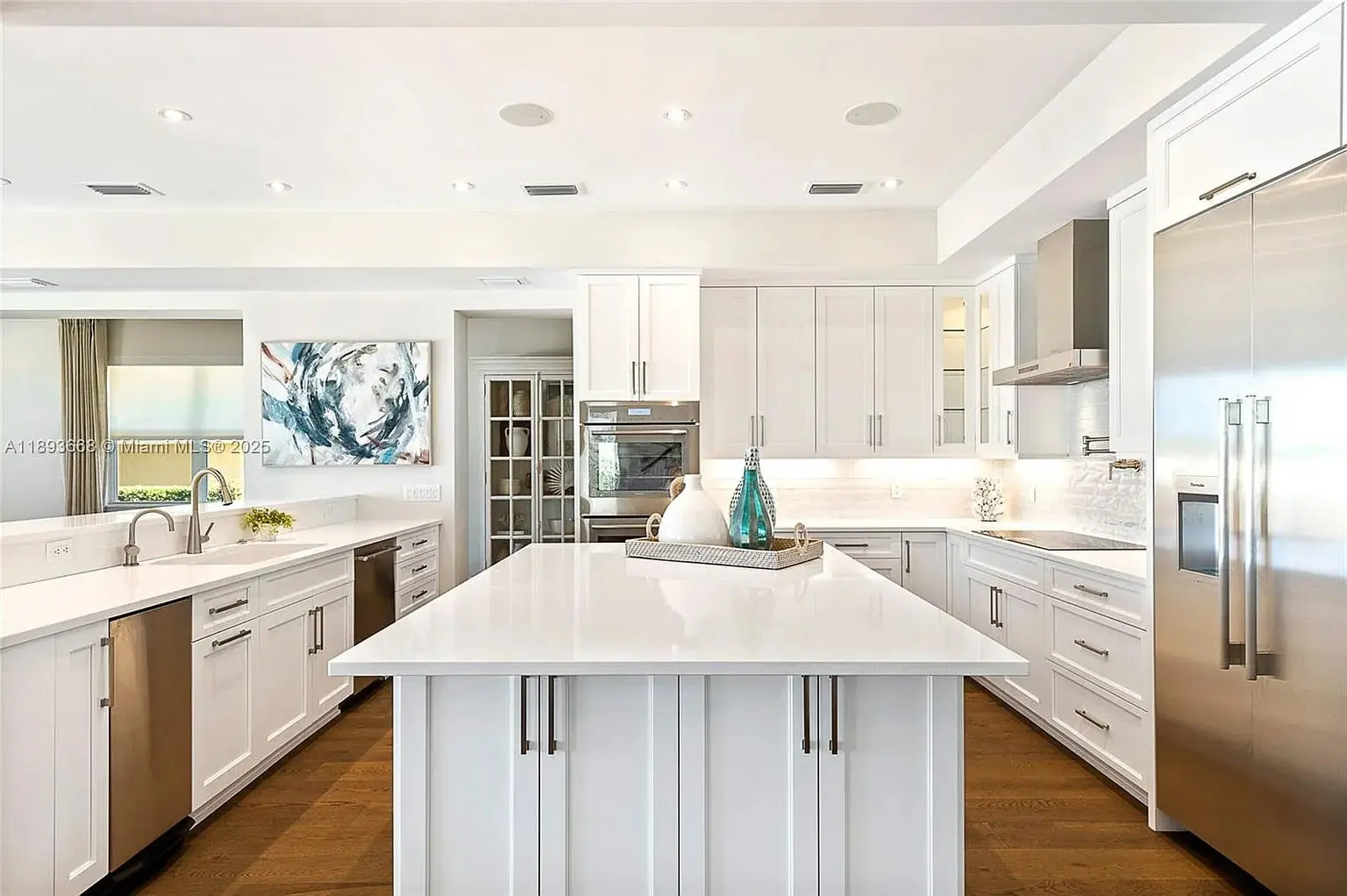 Modern kitchen with white cabinets, large island, stainless steel appliances, and wooden floor.