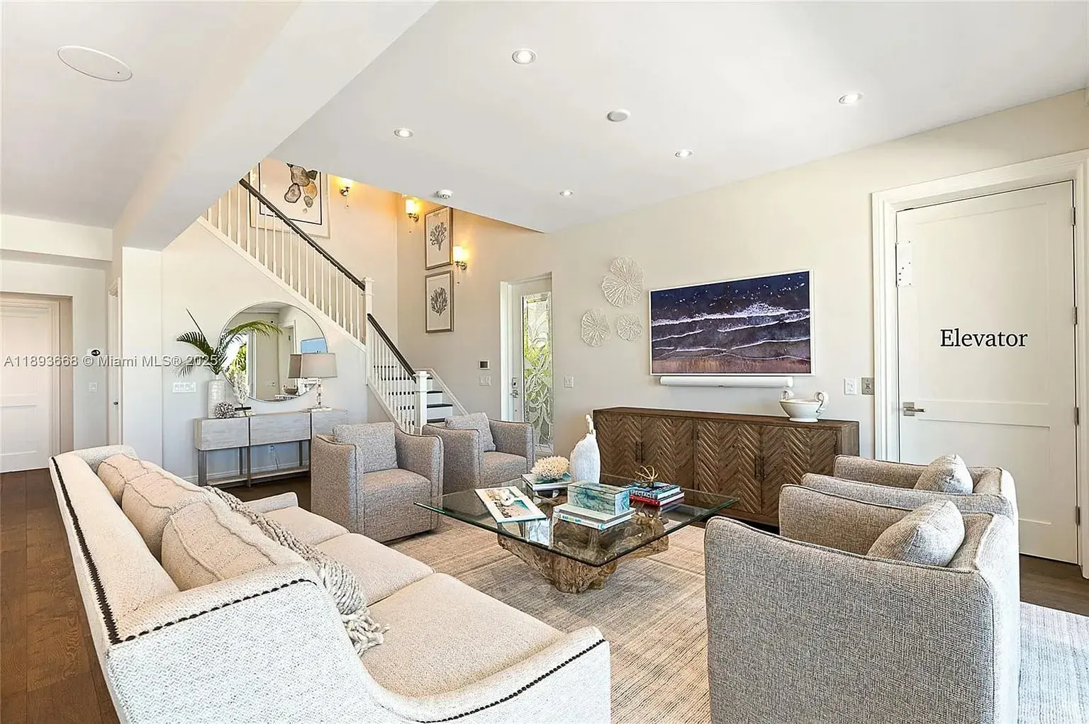 Modern living room with neutral tones, plush seating, glass coffee table, and wall-mounted TV.