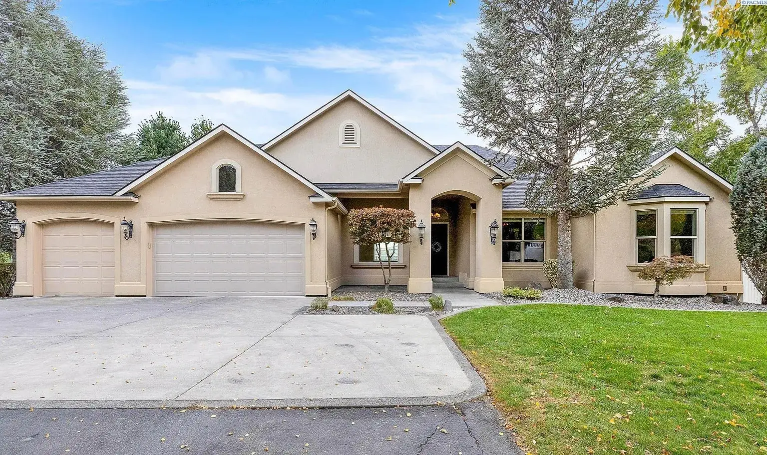 Single-story beige house with three-car garage, arched entryway, and surrounding trees.