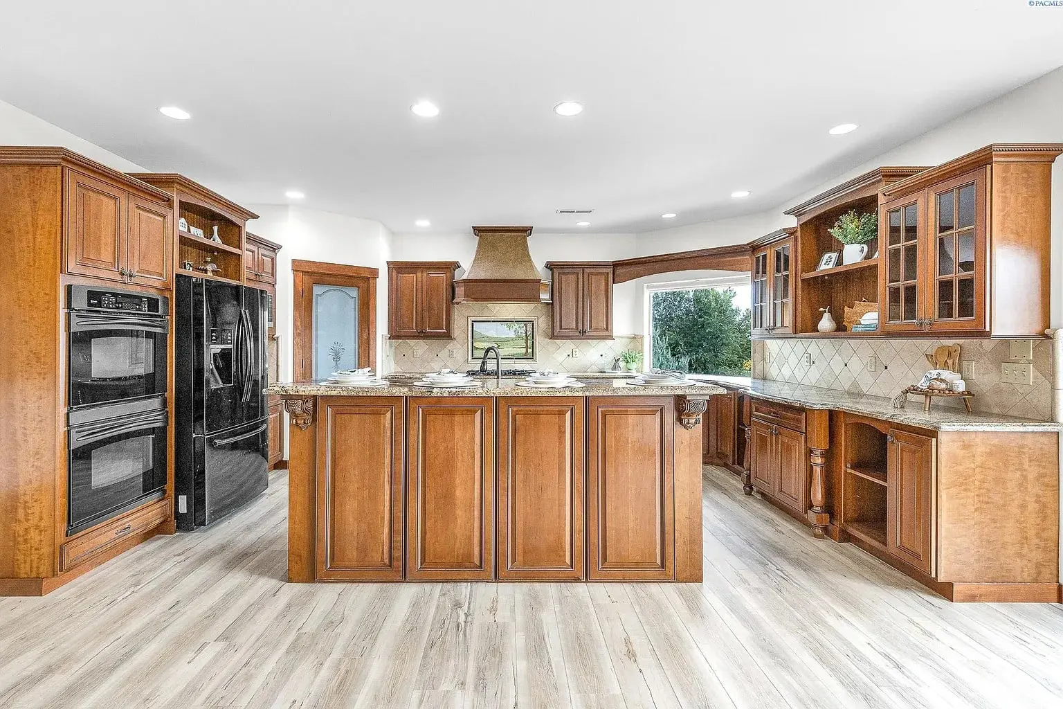 Spacious kitchen with wooden cabinets, central island, double ovens, and large windows.