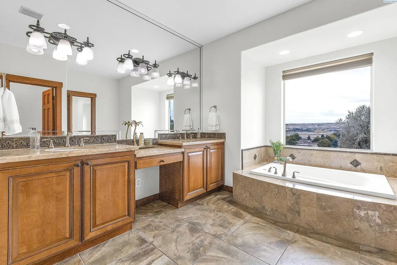 Spacious bathroom with wooden cabinets, large mirror, and a bathtub by a window with a view.