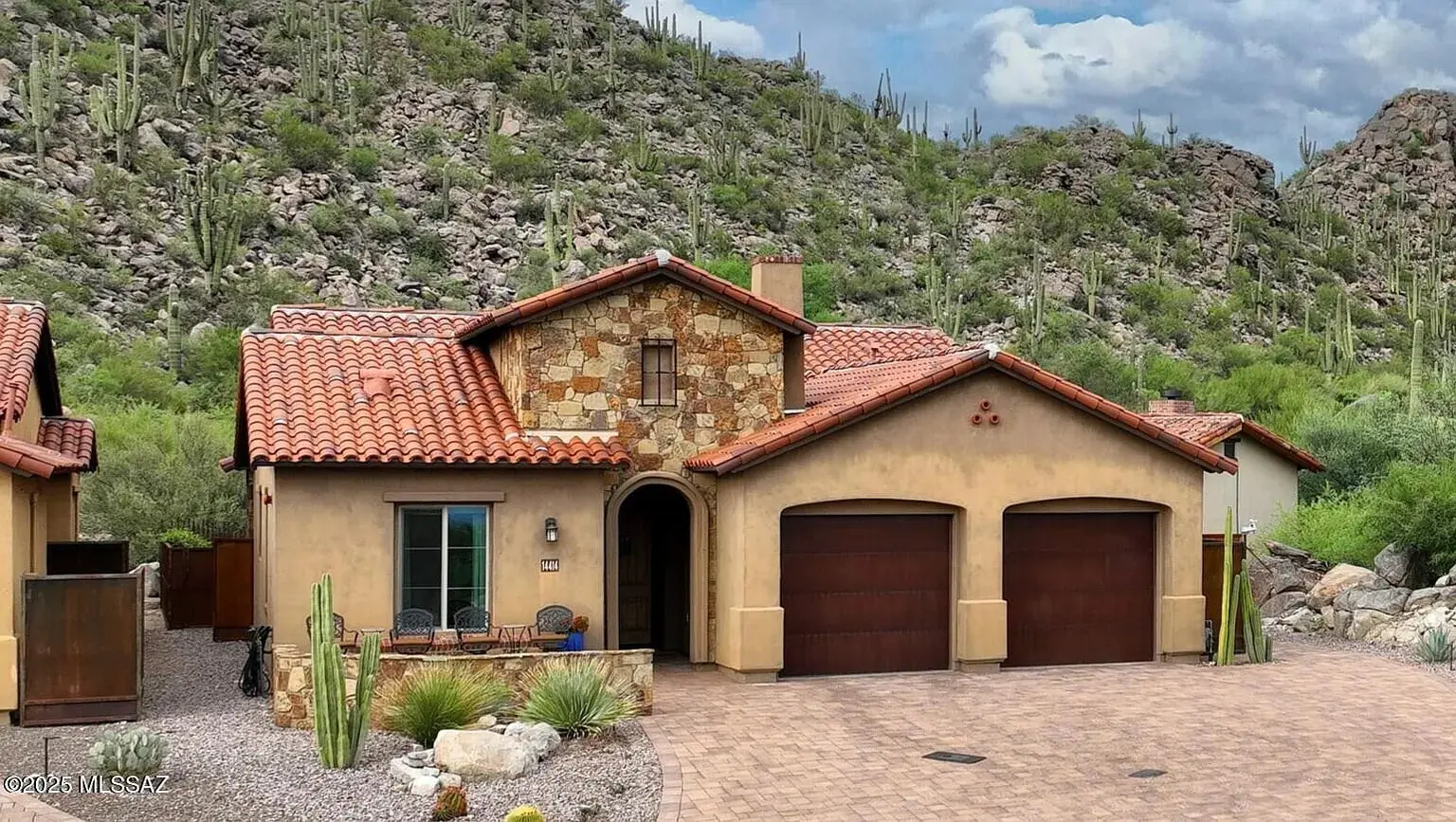 Single-story house with stone accents, red tile roof, and desert landscaping in a mountainous area.