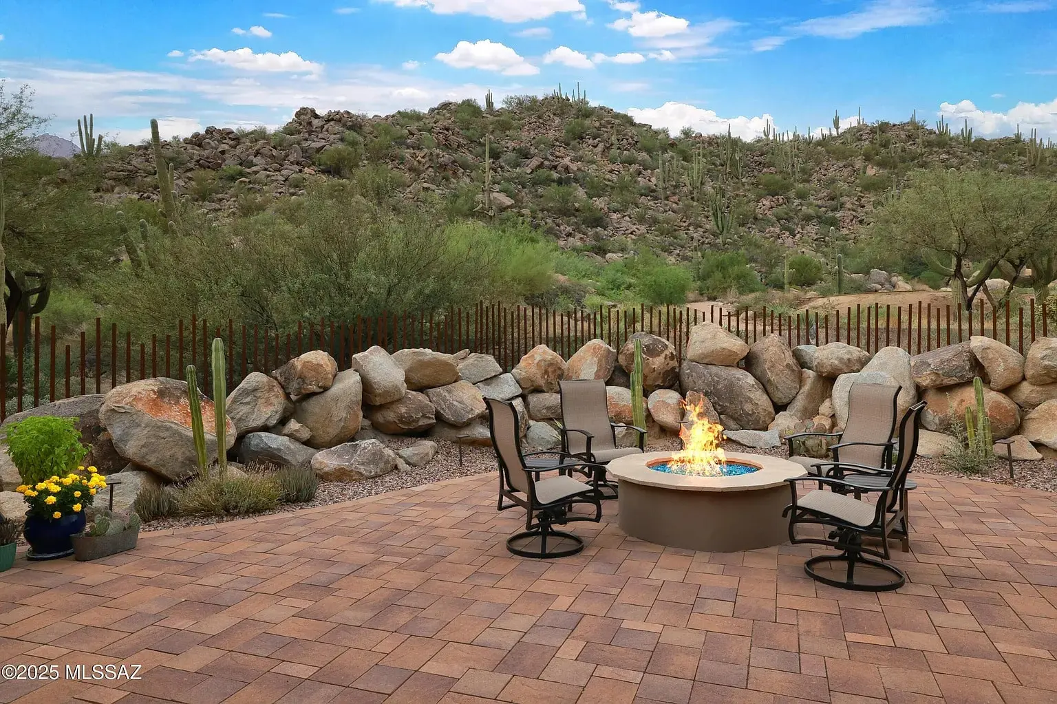 Patio with fire pit, surrounded by chairs, desert landscape, and rocky hills in the background.