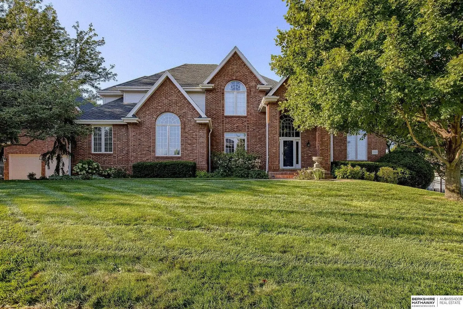 Large brick house with multiple gables, surrounded by a well-maintained lawn and trees.