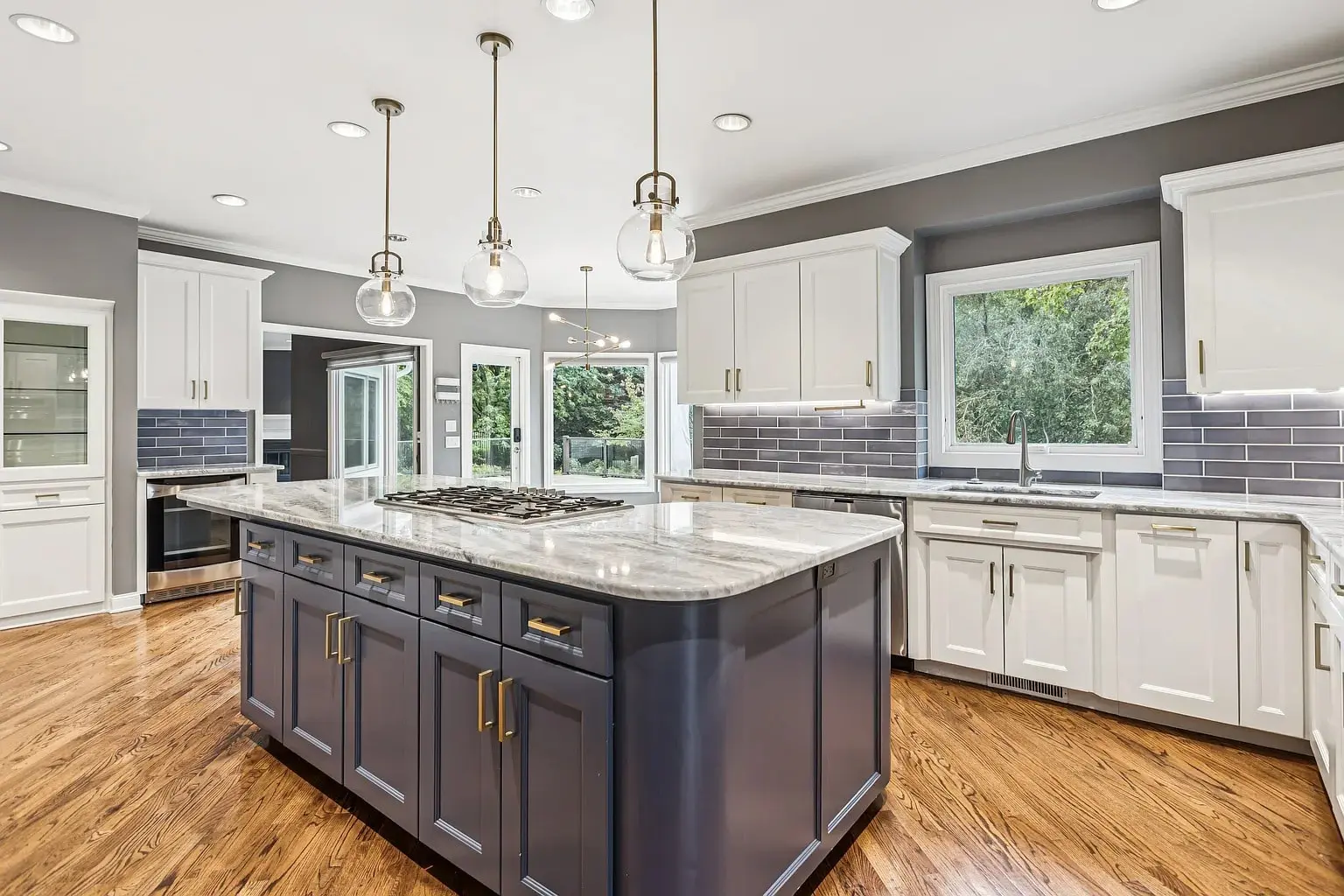 Modern kitchen with a large island, pendant lights, white cabinets, and hardwood floors.