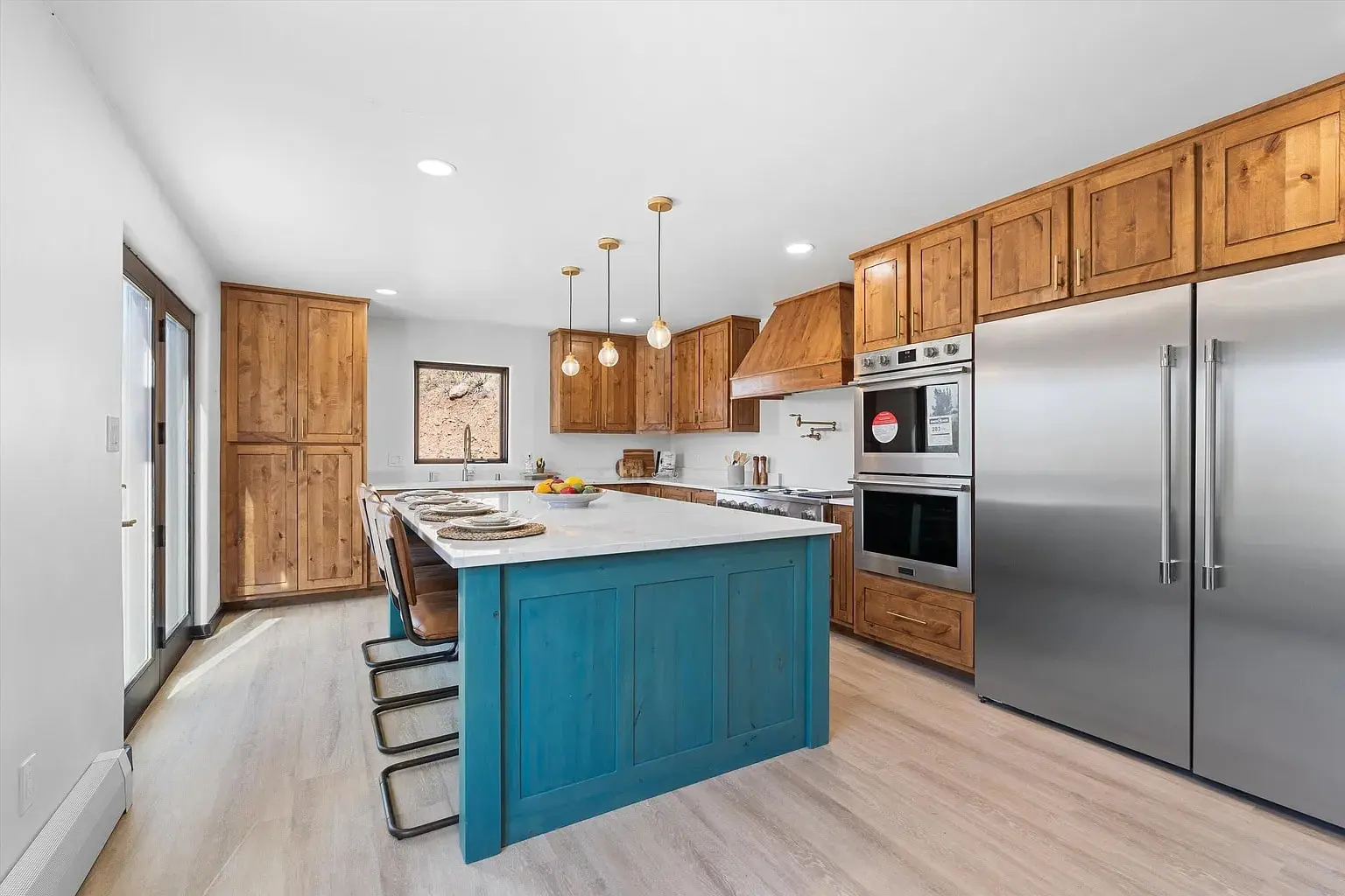 Modern kitchen with wooden cabinets, blue island, stainless steel appliances, and pendant lights.