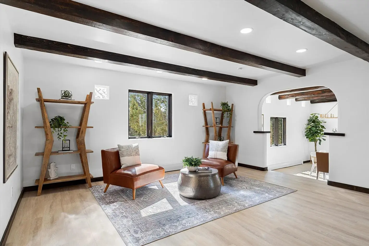 Living room with wooden beams, leather chairs, a round table, and a large window.