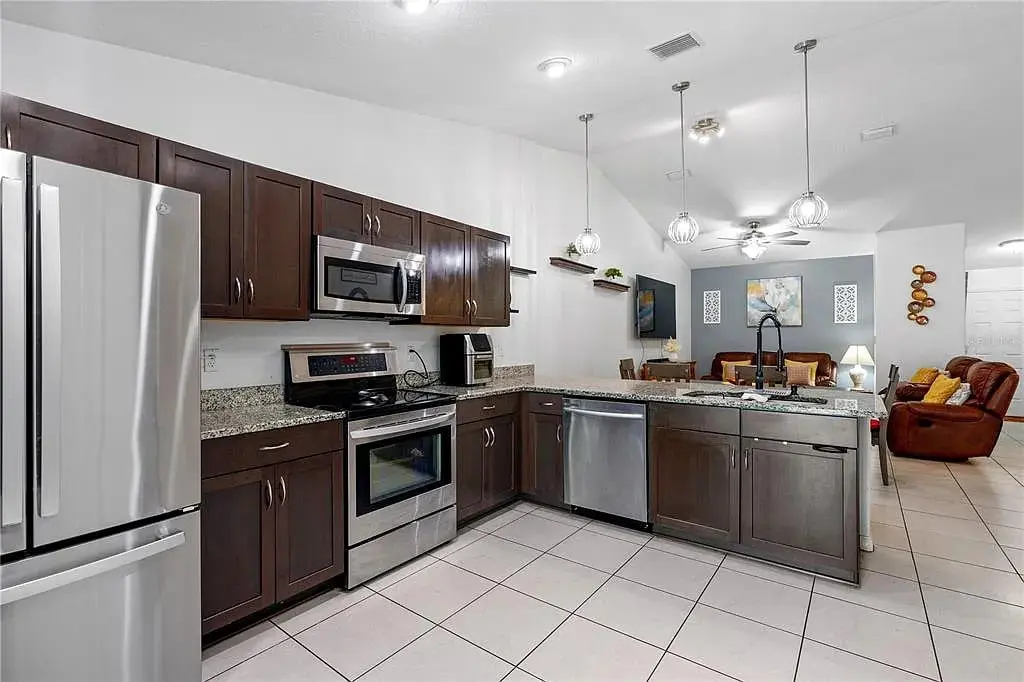 Modern kitchen with stainless steel appliances, dark wood cabinets, and open view to living area.