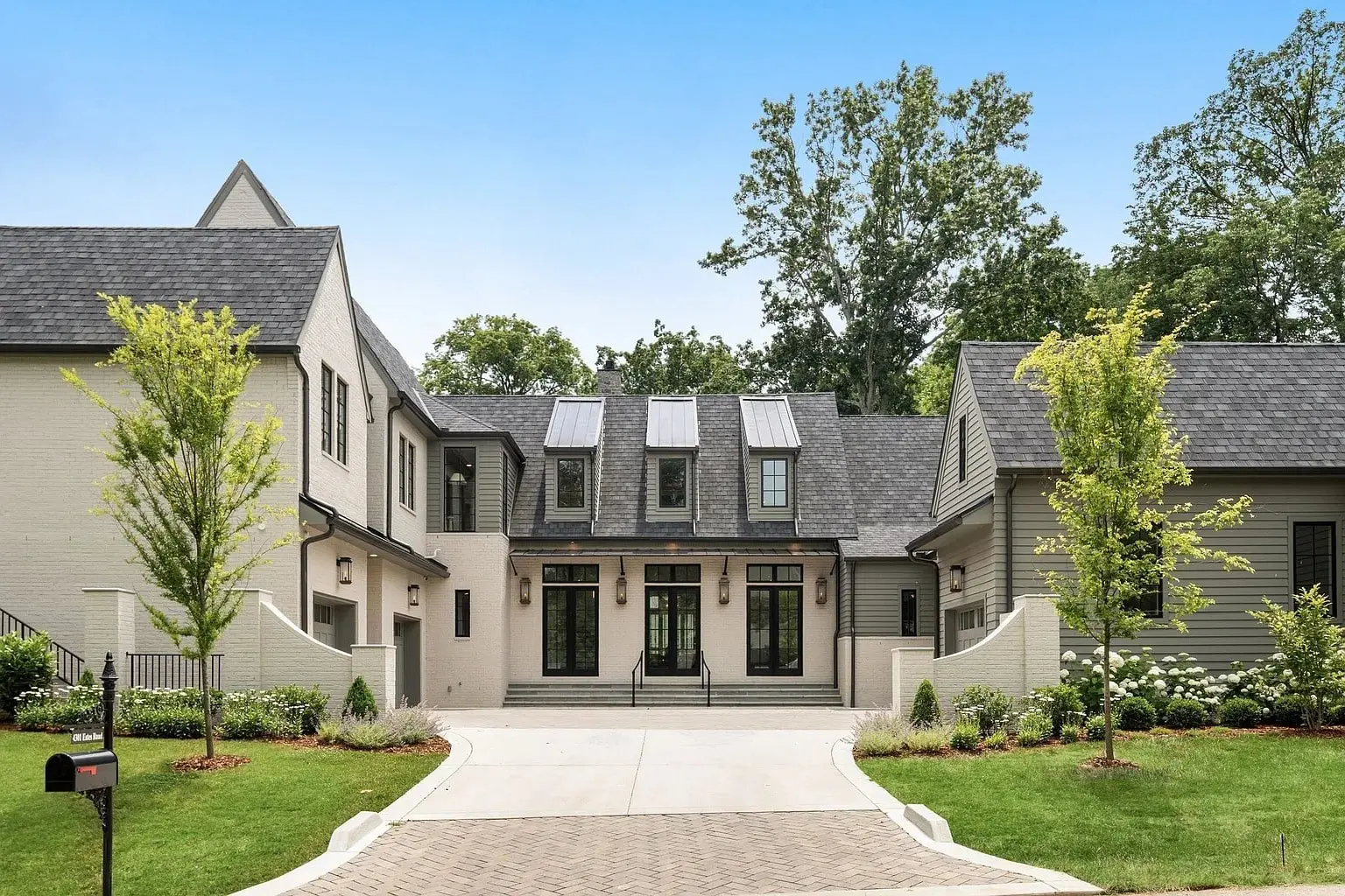 Modern two-story house with large windows, surrounded by trees and a paved driveway.