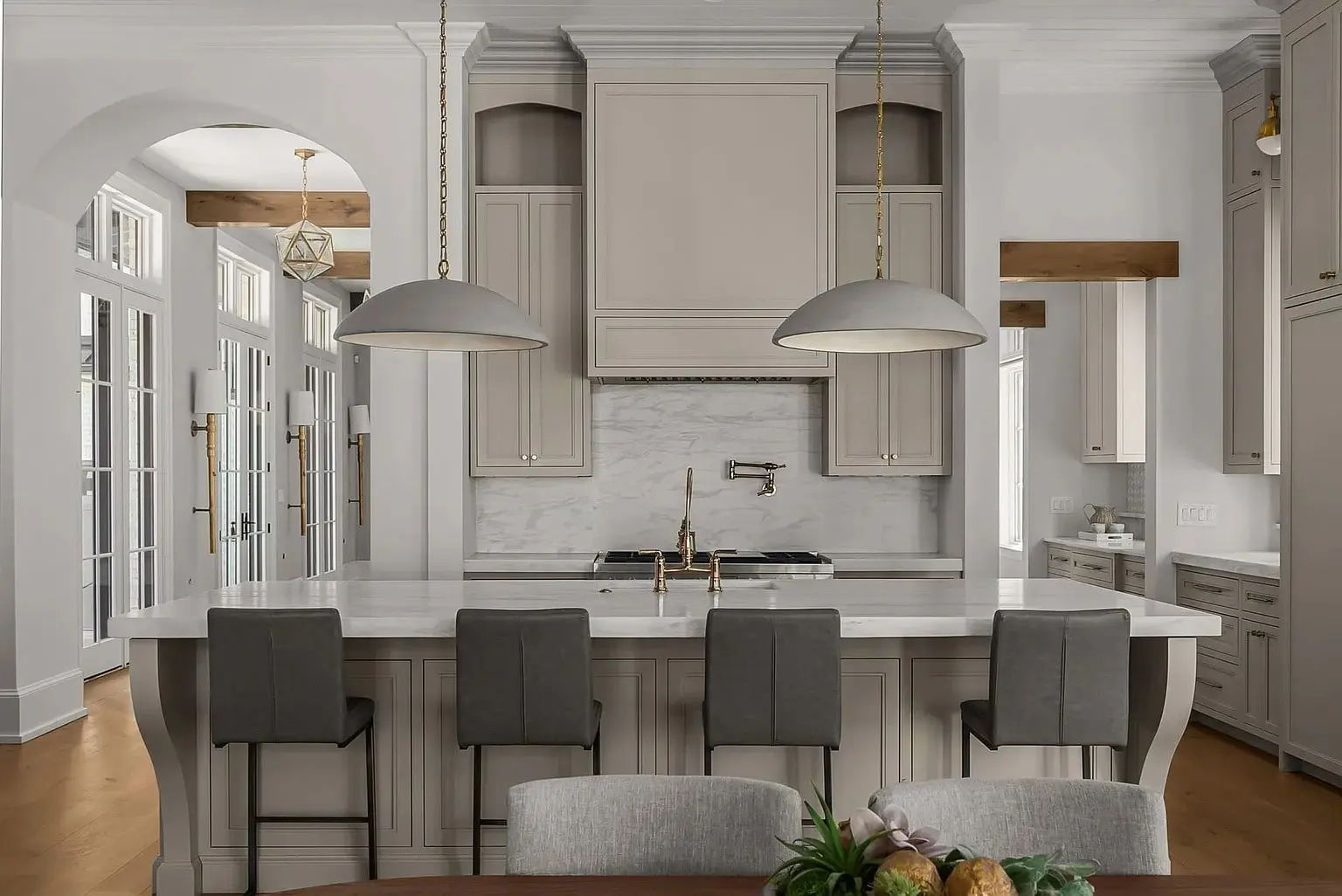 Modern kitchen with a large island, pendant lights, and high-backed chairs. Neutral color scheme.