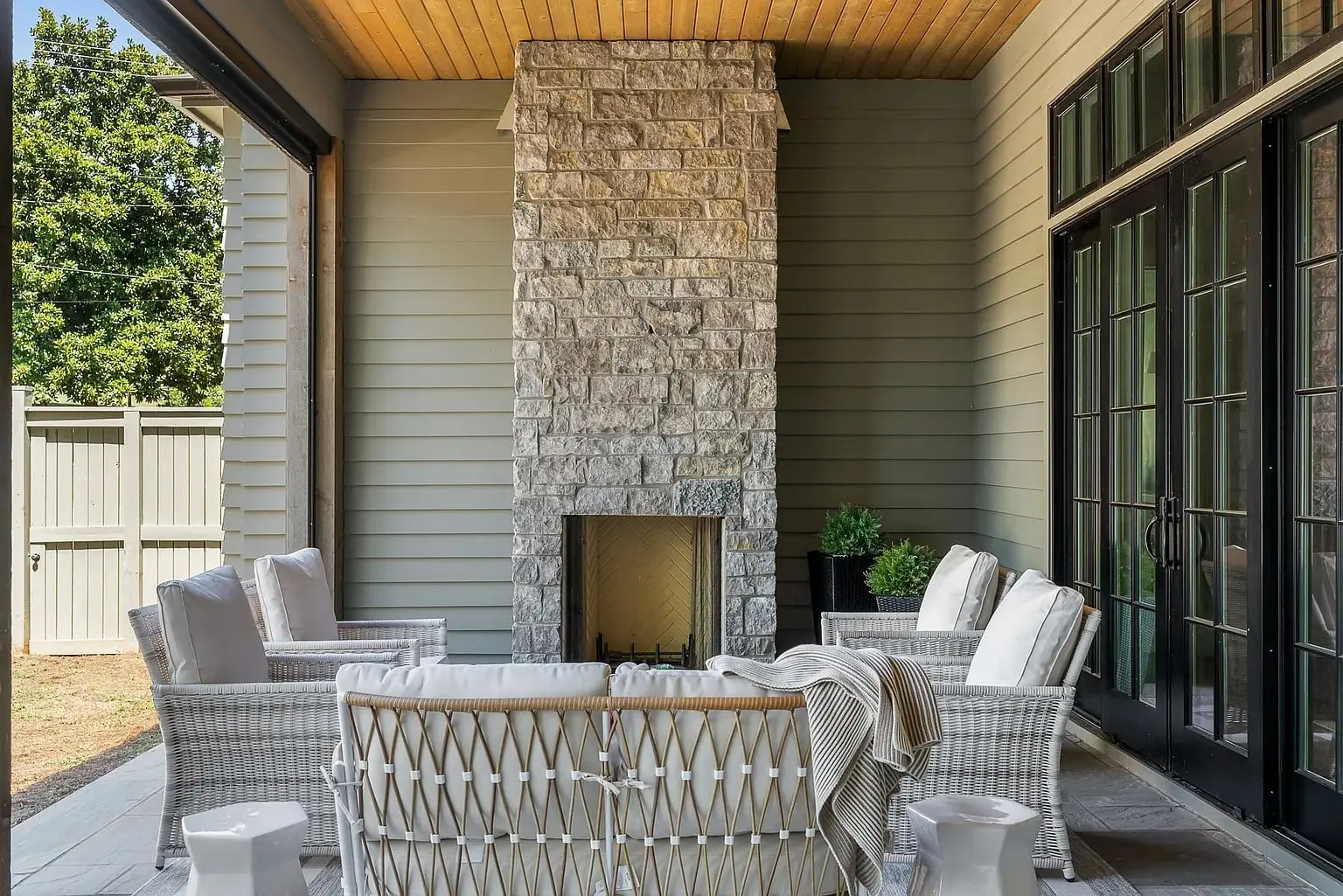 Outdoor patio with wicker furniture and a stone fireplace, surrounded by light gray walls.