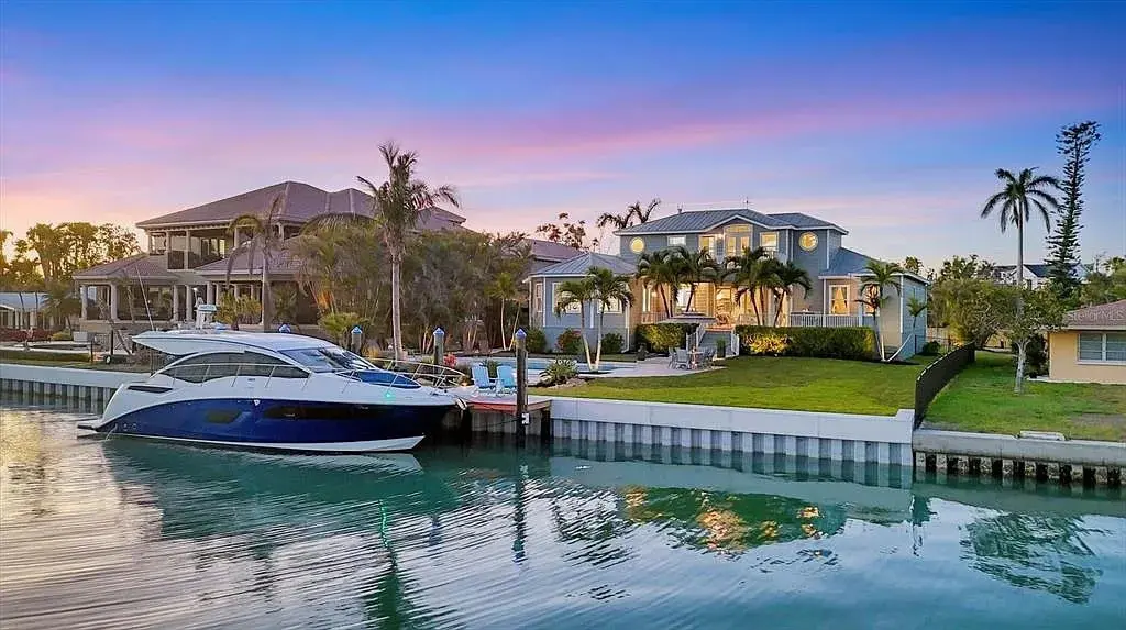 Waterfront property with a boat docked, surrounded by palm trees, under a colorful sunset sky.