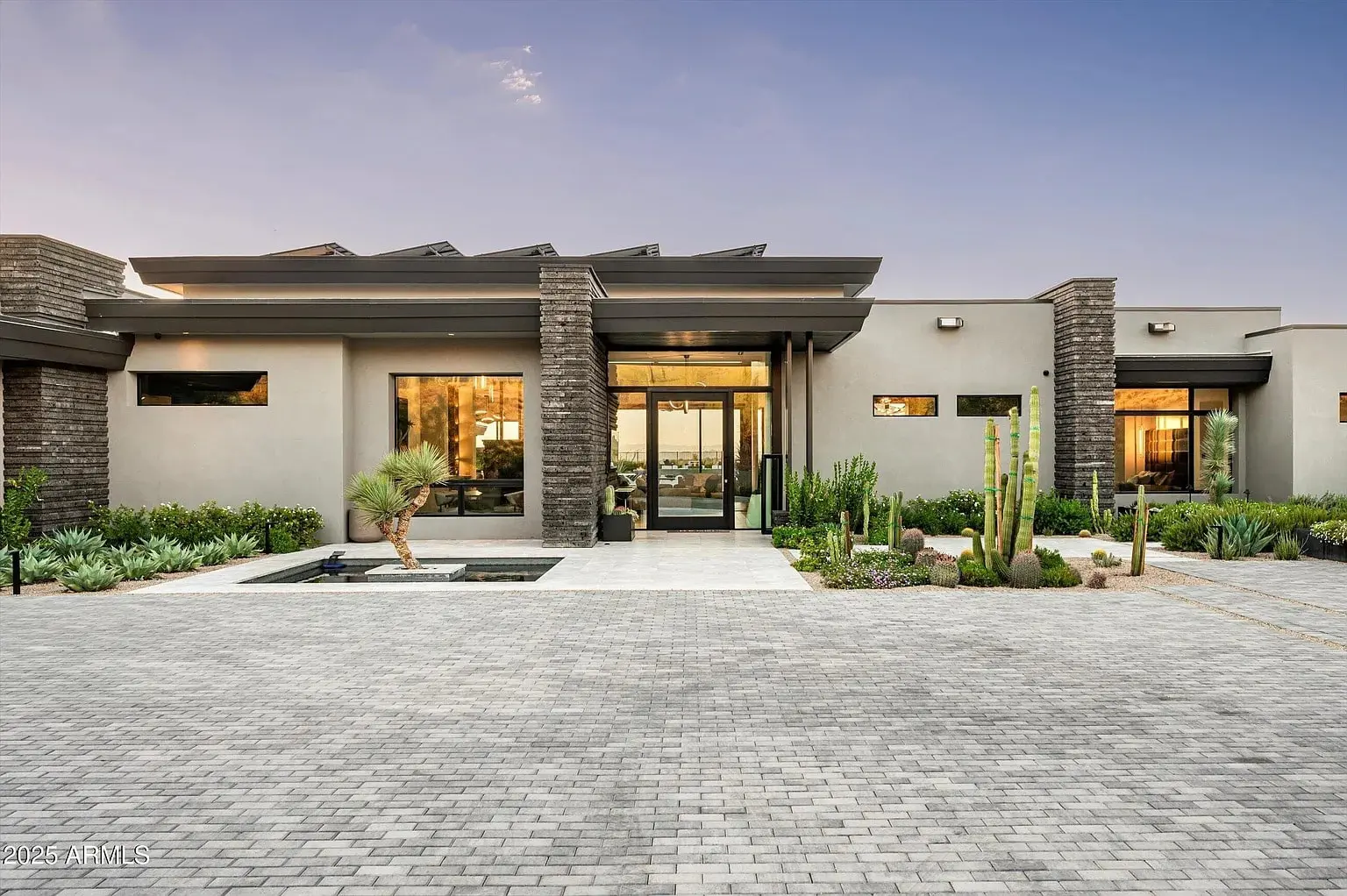 Modern house with large windows, stone accents, and landscaped front yard at sunset.