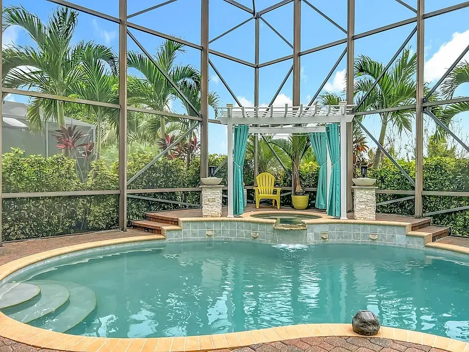 Enclosed backyard pool with a pergola, yellow chair, and tropical plants.