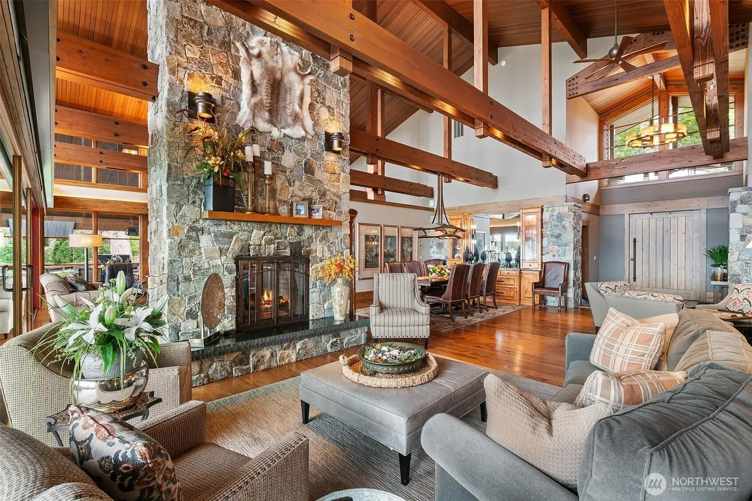 Spacious living room with stone fireplace, wooden beams, and large windows in a rustic style home.