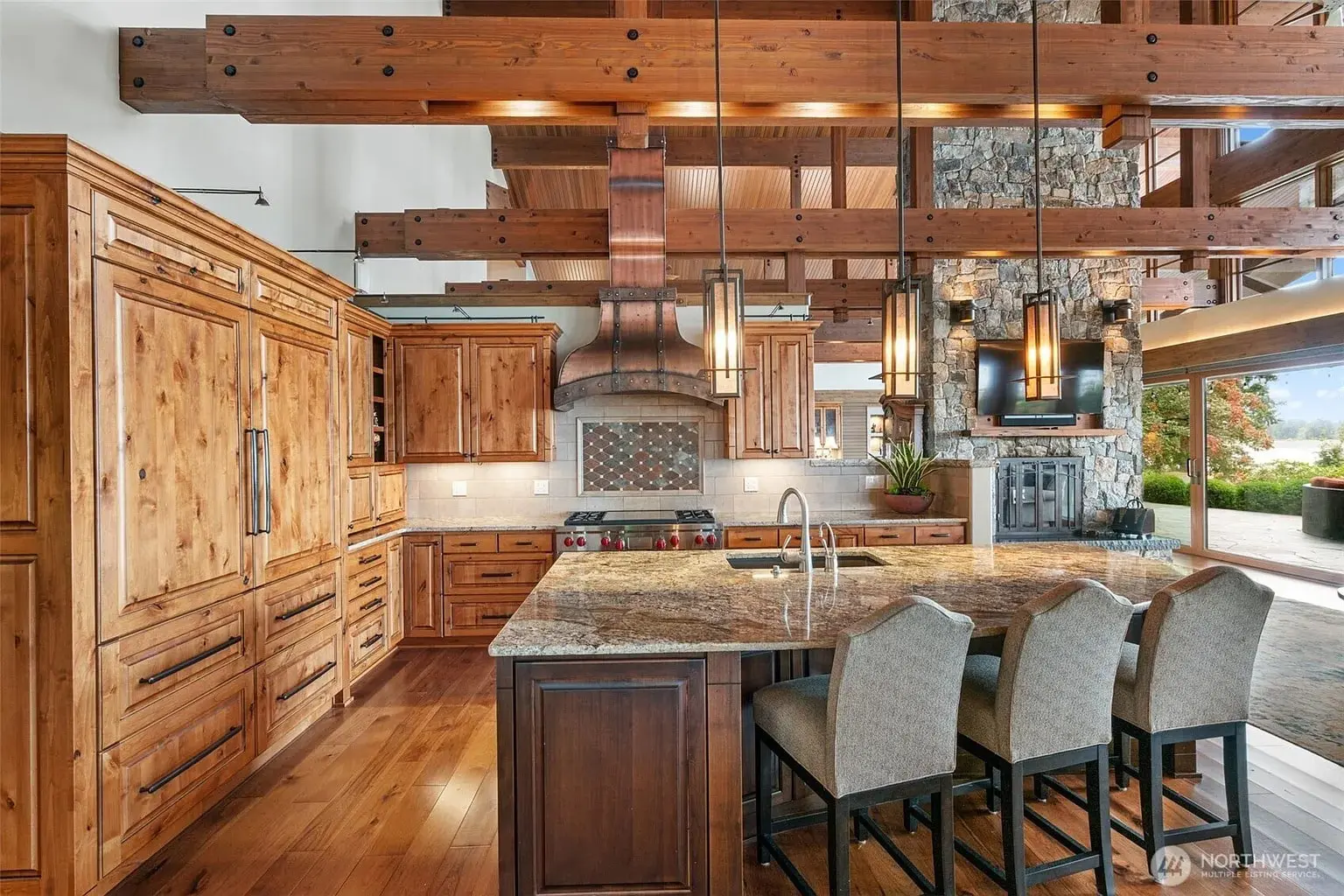 Rustic kitchen with wooden cabinets, exposed beams, stone accents, and a large island with chairs.