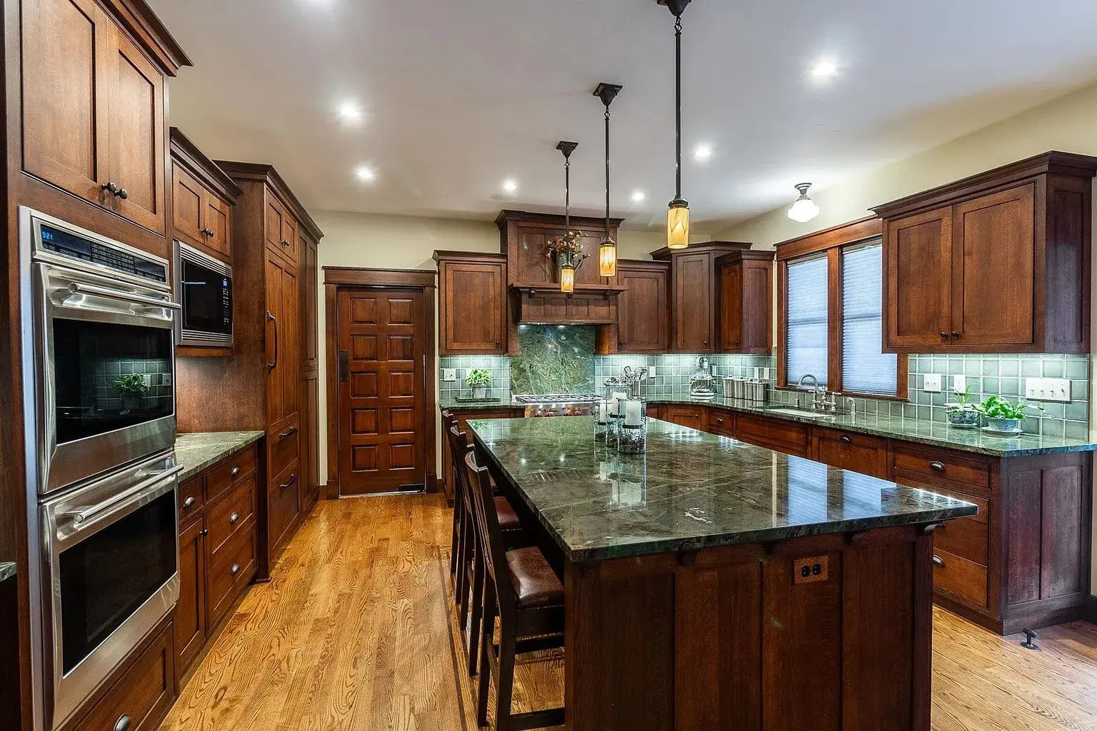 Spacious kitchen with wooden cabinets, marble countertops, and modern appliances, featuring an island and pendant lights.