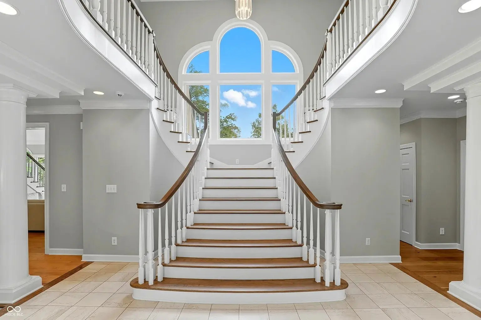 Grand staircase with dual curved railings, large arched window, and neutral-toned interior.