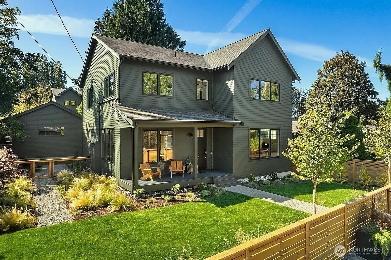 Two-story green house with a porch, surrounded by a landscaped yard and trees.