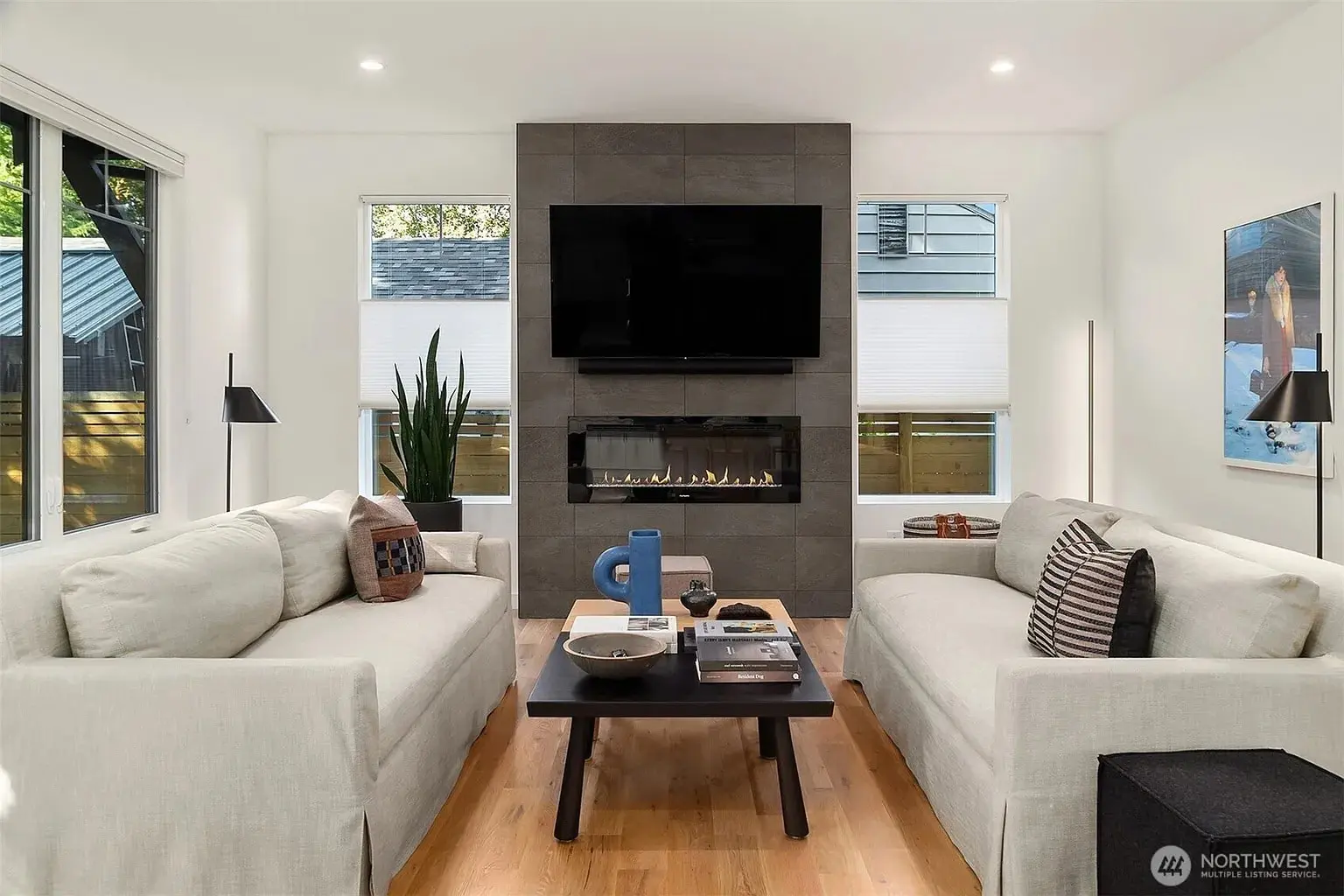 Modern living room with two sofas, a central coffee table, and a wall-mounted TV above a fireplace.