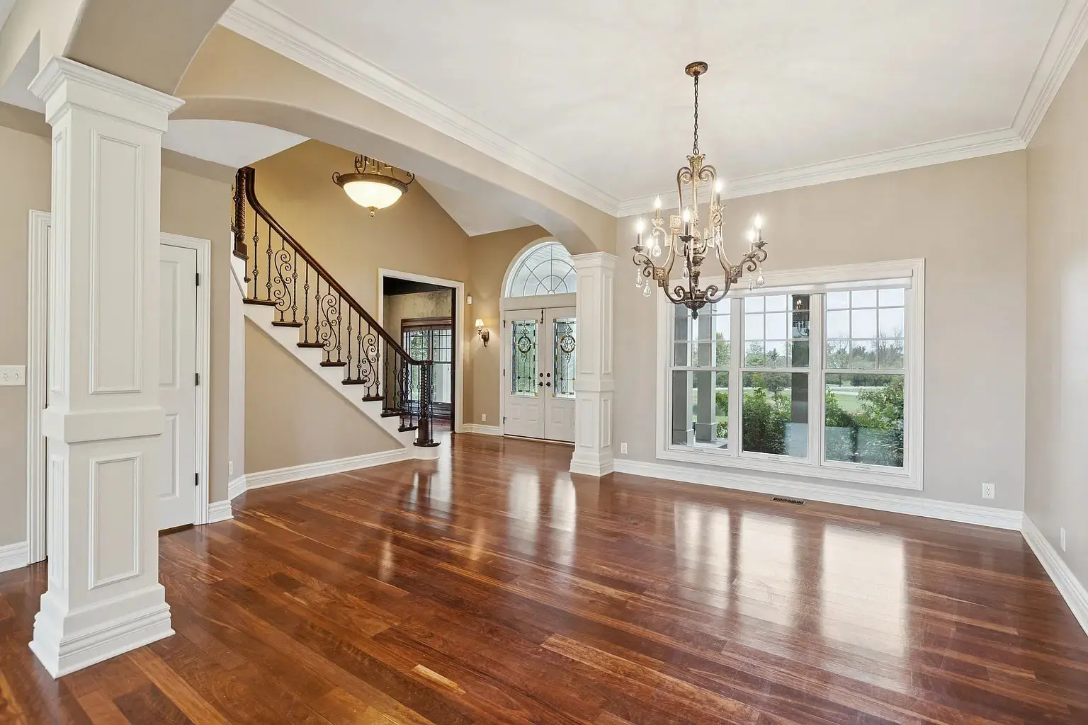 Spacious, elegant foyer with hardwood floors, chandelier, large windows, and a staircase with wrought iron railing.