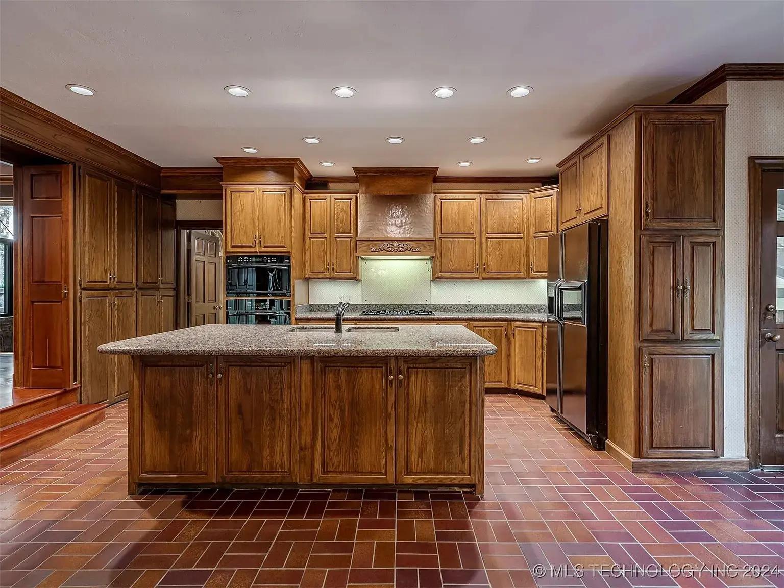 Spacious kitchen with wooden cabinets, central island, stainless steel appliances, and brick-patterned floor.